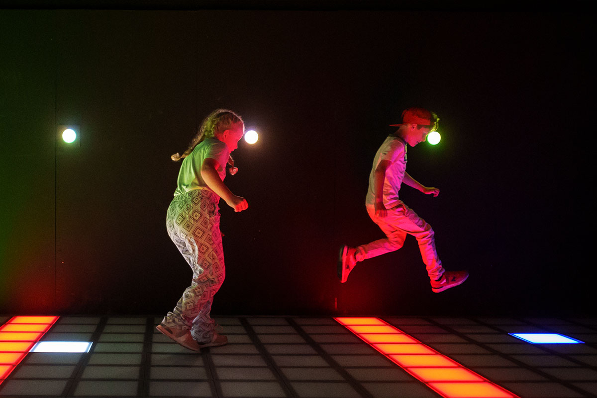 Zwei kinder springen ueber bunte felder am led fussboden der pixel games